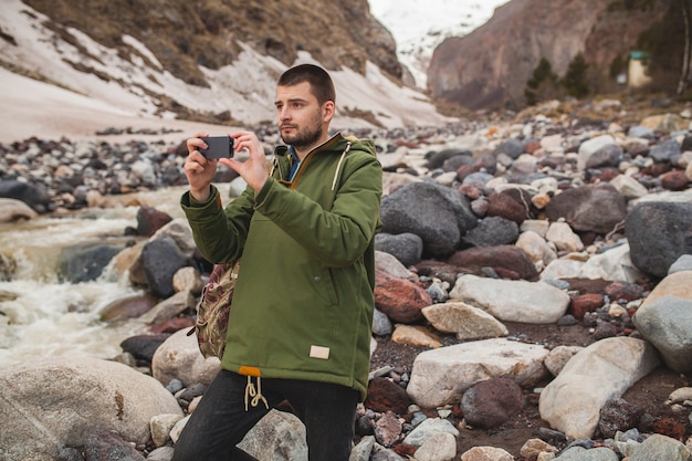 Homem jovem hippie tirando fotos com smartphone, natureza selvagem, férias de inverno, caminhadas