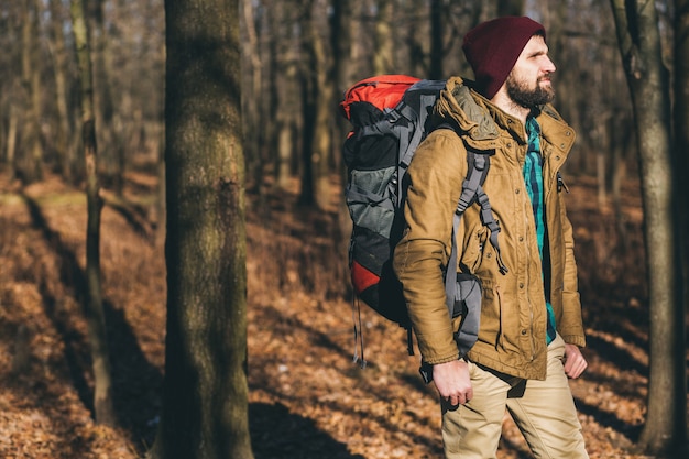 Homem jovem hippie viajando com mochila na floresta de outono, vestindo jaqueta e chapéu, turista ativo, explorando a natureza na estação fria