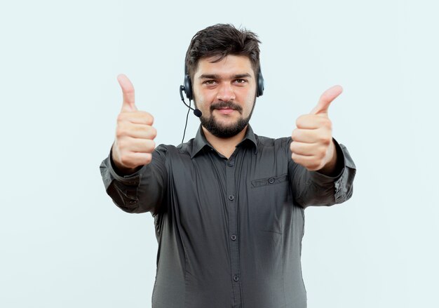 Homem jovem satisfeito com o call center usando fone de ouvido com o polegar para cima, isolado no fundo branco