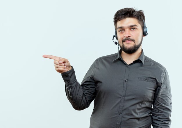 Homem jovem satisfeito do call center usando pontas de fone de ouvido na lateral, isolado no fundo branco com espaço de cópia