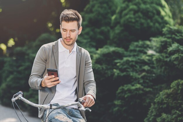 Homem jovem, sentando, ligado, bicicleta, olhar, smartphone