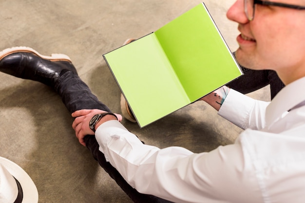 Homem jovem, sentar chão concreto, segurando, um livro aberto, em, mão