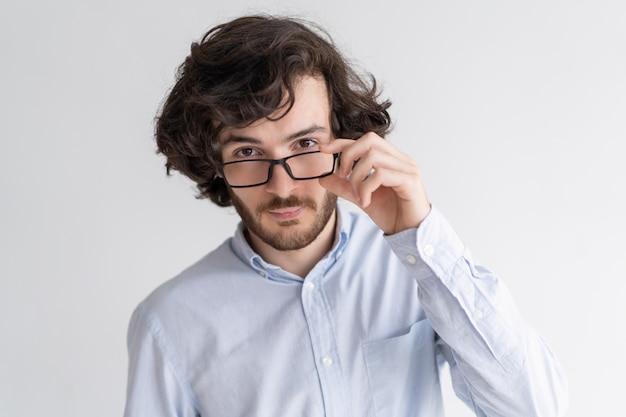 Homem jovem sério, olhando para a câmera por cima de óculos