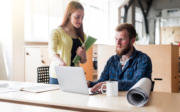 Homem jovem, trabalhar, laptop, com, colegas, escrivaninha, em, escritório