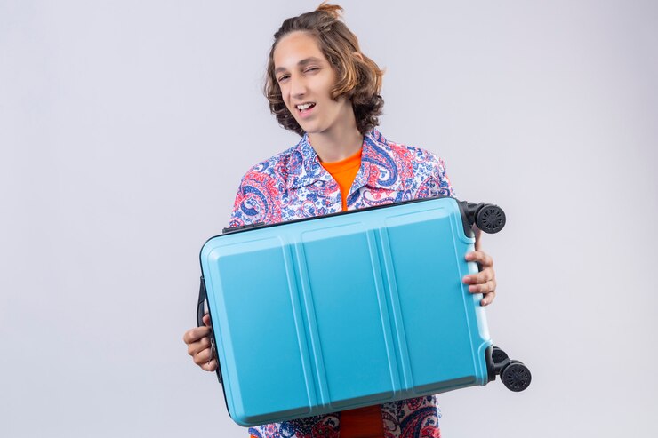 Foto grátis homem jovem viajante com mala azul, olhando confiante, sorrindo com cara feliz pronta para viajar em pé