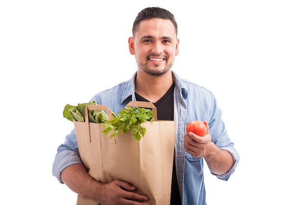 Homem latino bonito carregando um saco de mantimentos e mostrando toda a comida saudável que ele acabou de comprar