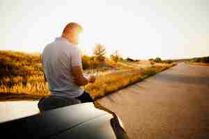 Foto grátis homem lendo um livro sentado no capô do carro