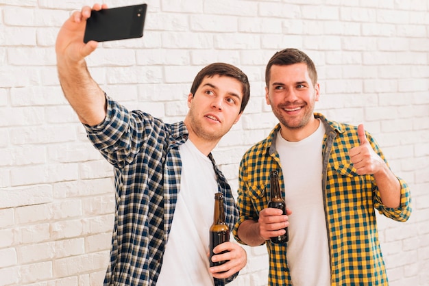 Foto grátis homem, levando, selfie, com, seu, amigo, ligado, smartphone, ficar, contra, parede branca tijolo