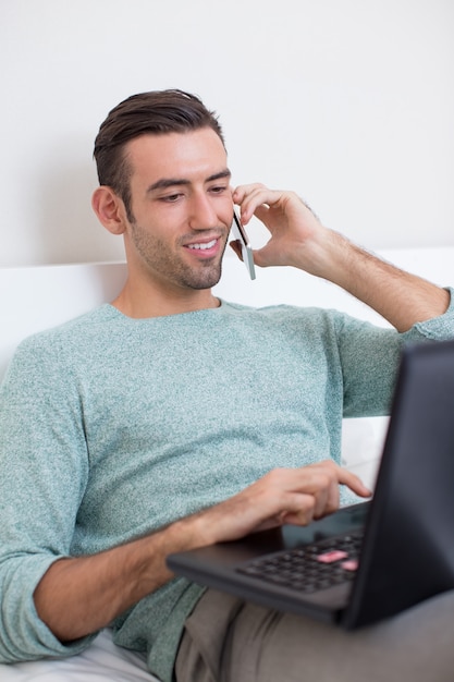 Homem ligando no telefone e trabalhando no laptop em casa