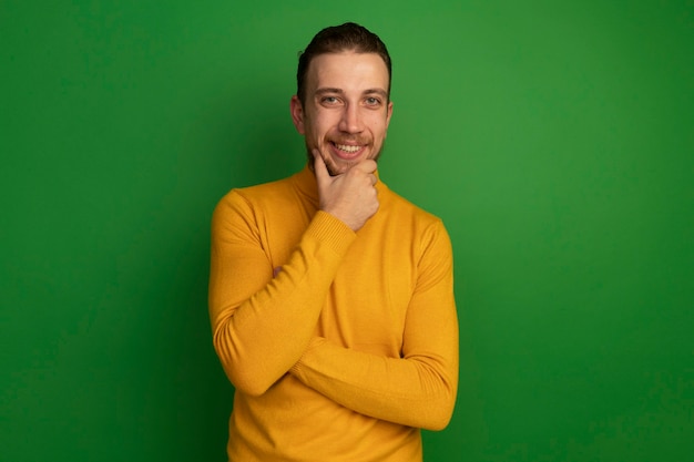 Homem loiro bonito sorridente segurando o queixo verde