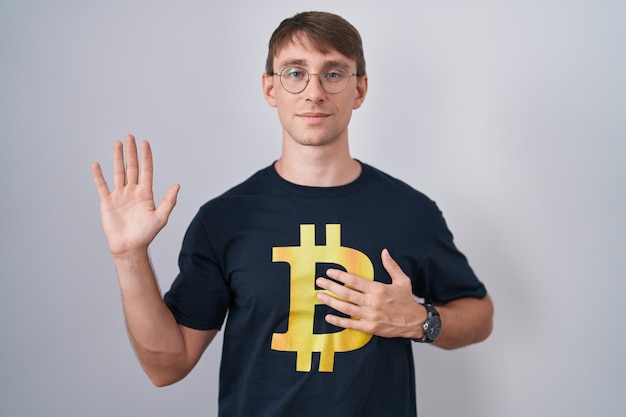 Foto grátis homem loiro caucasiano vestindo camiseta bitcoin xingando com a mão no peito e a palma da mão aberta, fazendo um juramento de promessa de lealdade