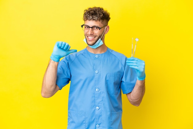 Homem loiro dentista segurando ferramentas isoladas no fundo orgulhoso e satisfeito Foto Premium