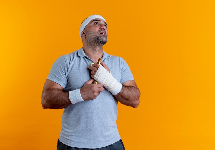 Foto grátis homem maduro e desportivo com uma bandana abraçando seu troféu, olhando para cima com expressão de esperança em pé sobre a parede laranja