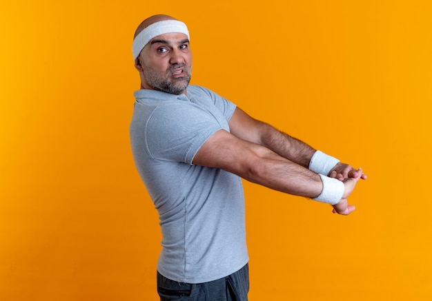 Foto grátis homem maduro e desportivo com uma bandana, esticando as mãos, parecendo confiante em pé sobre a parede laranja