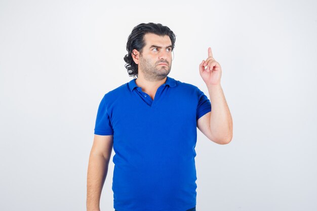 Homem maduro, levantando o dedo indicador em gesto de eureka em camiseta azul, jeans e parecendo sensato, vista frontal.