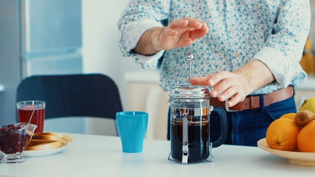 Homem mais velho fazendo café usando a imprensa francesa no café da manhã na cozinha. Idoso pela manhã desfrutando de cafeína de café expresso café marrom fresco de caneca vintage, filtro relaxante refresco