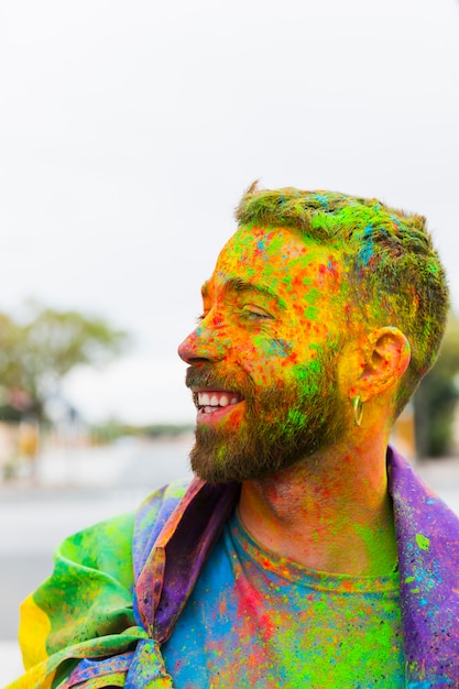 Homem manchado de tinta em pó com bandeira de arco-íris, sorrindo na rua