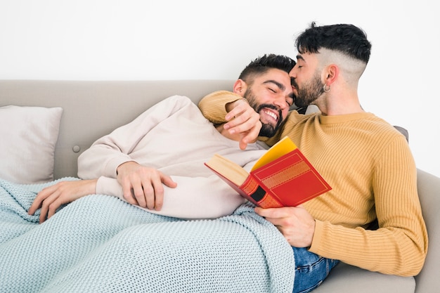 Homem, mentindo, ligado, sofá, beijando, seu, boyfriend&#39;s, testa, segurando livro, em, mão