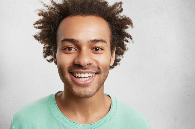 Homem mestiço alegre com cerdas, penteado espesso e dentes brancos perfeitos, tem bom humor
