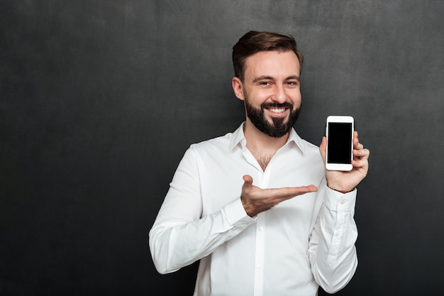 Homem morena positivo mostrando smartphone na câmera demonstrando ou publicidade gadget sobre espaço de cópia de grafite