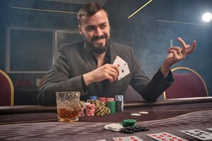 Homem moreno atrevido em um terno clássico está jogando pôquer sentado à mesa no cassino em um cigarro. ele está fazendo apostas esperando por uma grande vitória. apostas por dinheiro. jogos de fortuna.