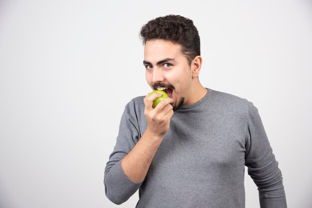 Homem moreno comendo maçã verde.