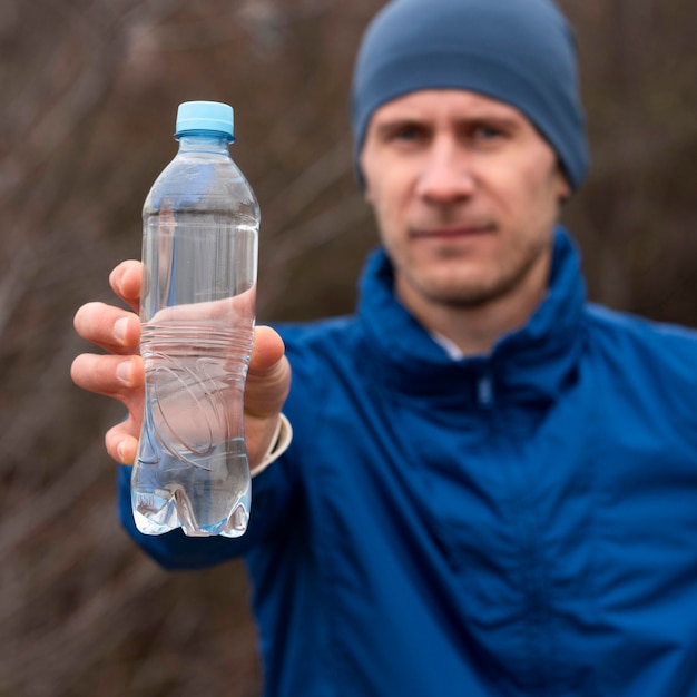 Homem mostrando garrafa de água na natureza