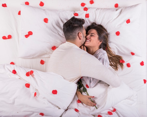 Homem, mulher abraçando, cama, com, pétalas rosa