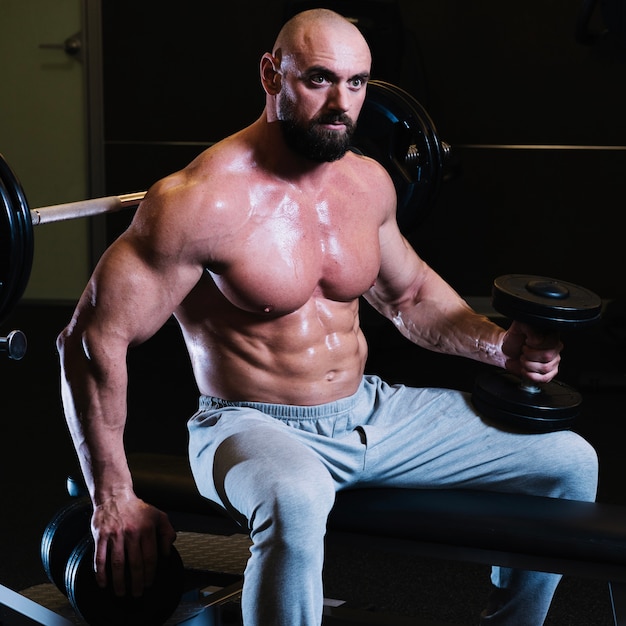 Homem musculoso descansando após levantar dumbbell