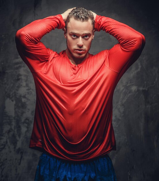 Homem musculoso em camiseta vermelha posando em fundo cinza.