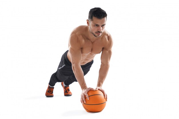 Homem musculoso fazendo flexões usando basquete.