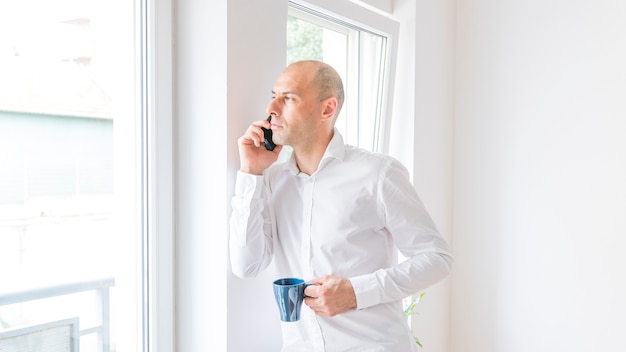 Homem negócios, falando, smartphone, olhar, através, escritório, janela