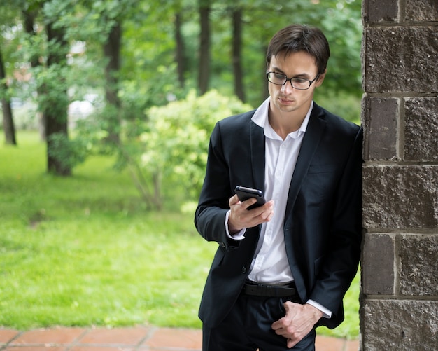 Homem negócios, inclinar-se parede, e, verificar, telefone