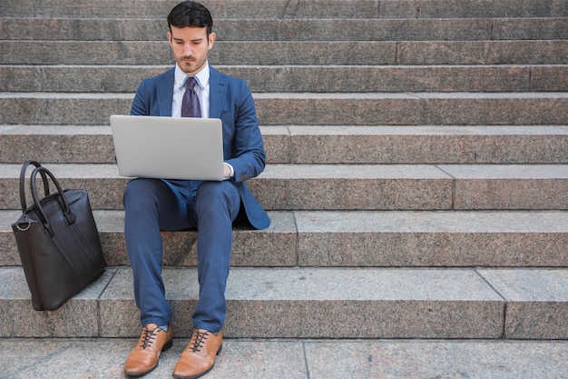 Homem negócios, usando computador portátil, perto, sacola