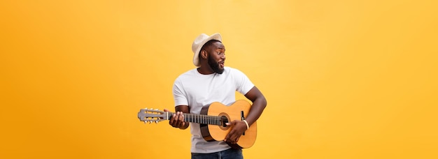 Homem negro musculoso tocando guitarra vestindo jeans e regata branca isolado sobre fundo amarelo