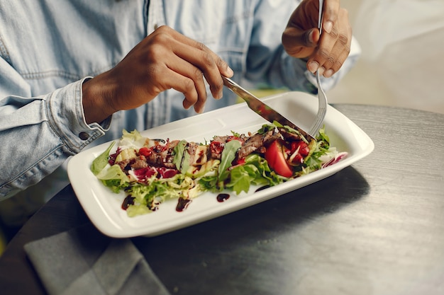 Homem negro sentado em um café e comer uma salada de legumes