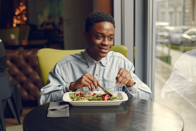 Homem negro sentado em um café e comer uma salada de legumes