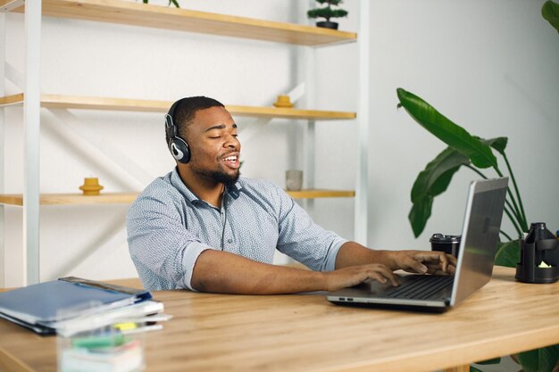 Homem negro sentado no escritório usando fones de ouvido e fazer uma chamada de vídeo