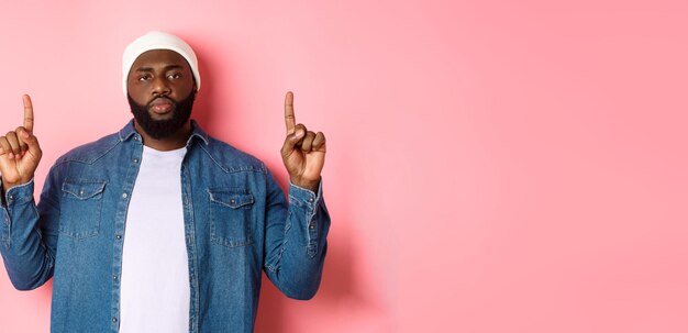 Foto grátis homem negro sério e incomodado com barba olhando para a câmera e apontando os dedos para cima mostrando promo st