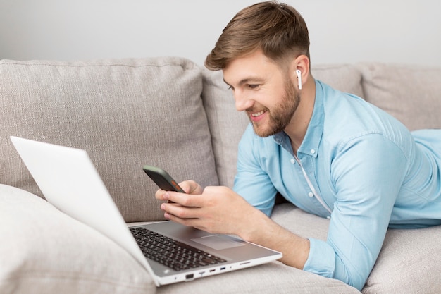 Homem no sofá com celular e laptop