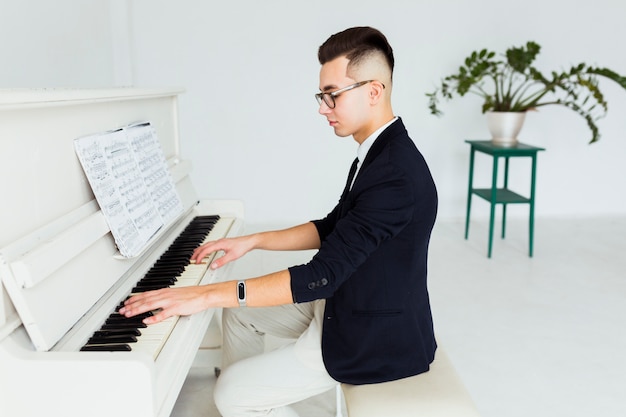 Homem novo considerável que joga o piano olhando a folha musical