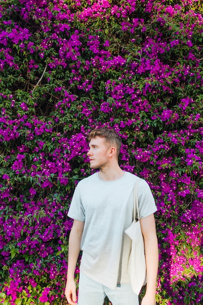 Foto grátis homem novo considerável que leva o saco de pano que está perto da árvore cor-de-rosa da flor