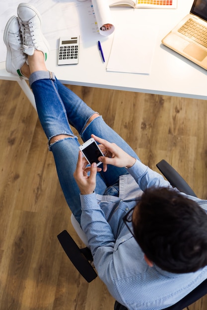 Homem novo considerável que usa seu telefone móvel no escritório.