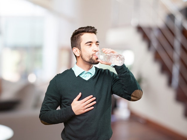 Homem novo que bebe água com uma mão no peito