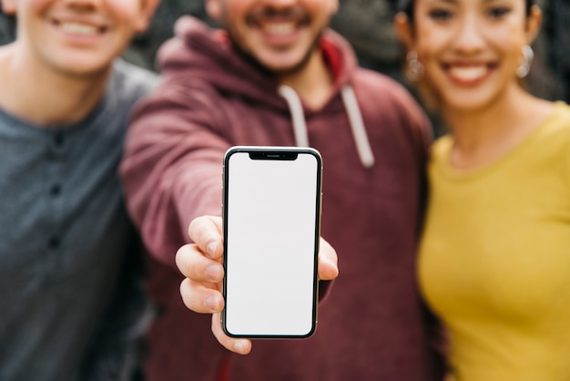 Homem novo que mostra o espaço vazio do smartphone ao estar perto dos amigos multirraciais