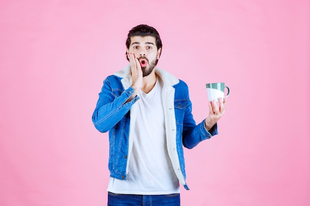 Homem olhando para sua xícara de café e mostrando uma expressão confusa