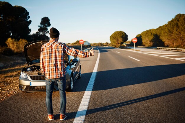 Homem parado ao lado de seu carro quebrado