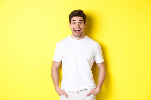 Homem parecendo surpreso, sorrindo espantado e olhando para o anúncio, em pé perto do espaço da cópia, fundo amarelo.