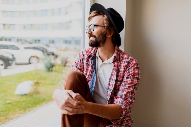 Homem pensativo com barba em óculos elegantes e roupa de primavera relaxante durante o dia de trabalho na empresa. Roupa de hipster.