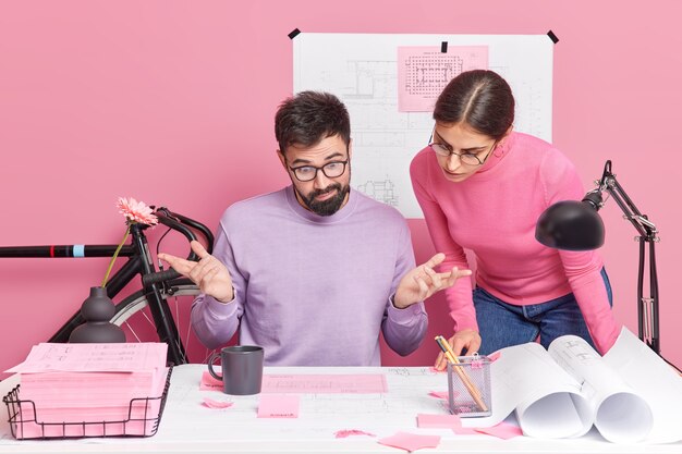 Homem perplexo espalha olhares confusos para papéis que sua colega posa perto de trabalhos juntos na planta do novo projeto discutem ideias para ilustração. Reunião de Brainstroming para engenharia.